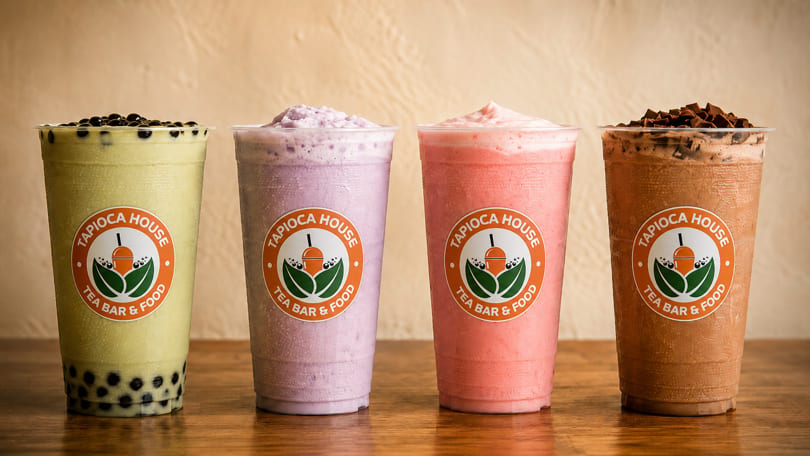 Four Tapioca House drinks: green boba, purple, pink, and chocolate smoothies on a wooden surface.
