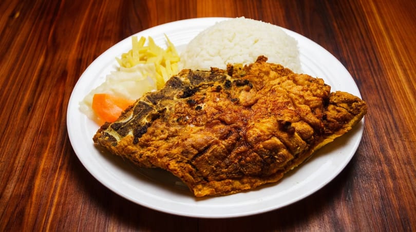 A whole golden fried fish, white rice, and pickled vegetables on a white plate.