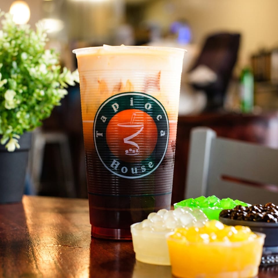 Tapioca House layered bubble tea with colorful boba and jellies on a wooden table.