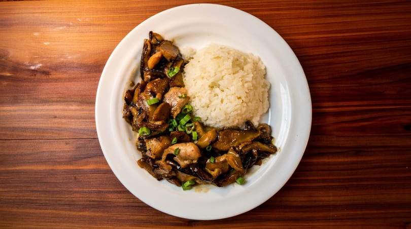 Chicken and mushroom stir-fry with white rice, garnished with green onions, on a white plate.